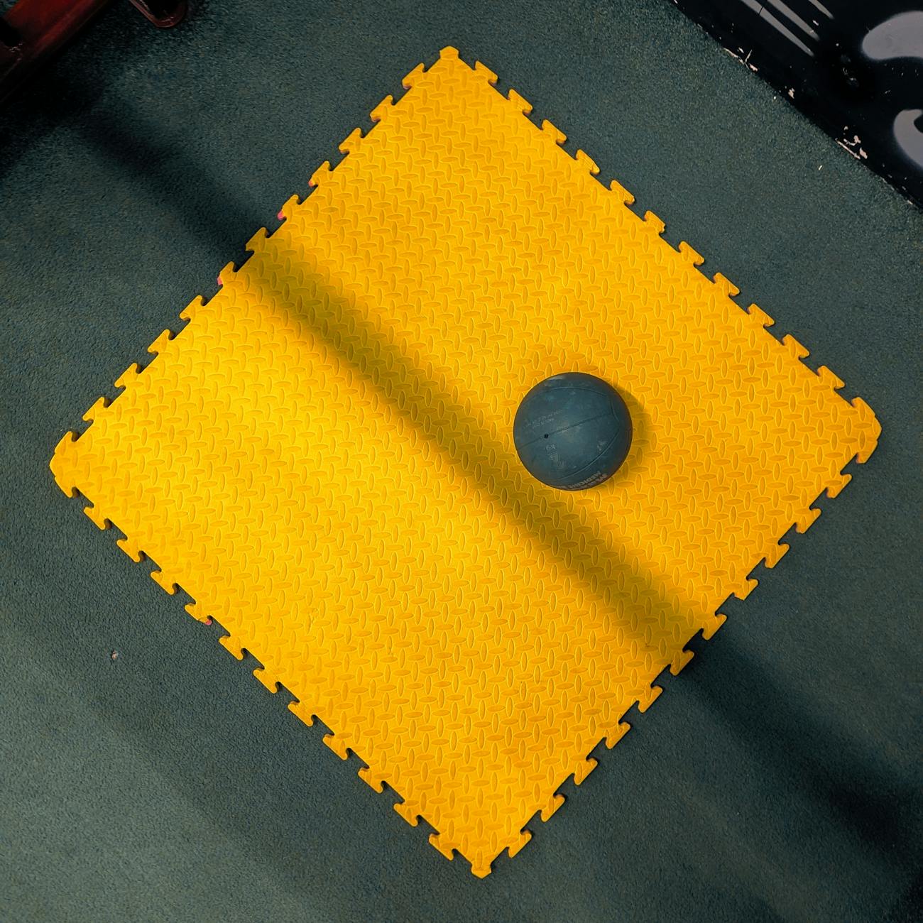 An overhead view of a yellow gym mat with a medicine ball in a gym setting, providing vibrant contrast.
