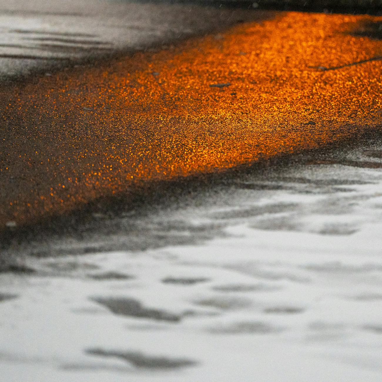 Orange streetlight glowing on wet pavement creating a moody urban reflection.