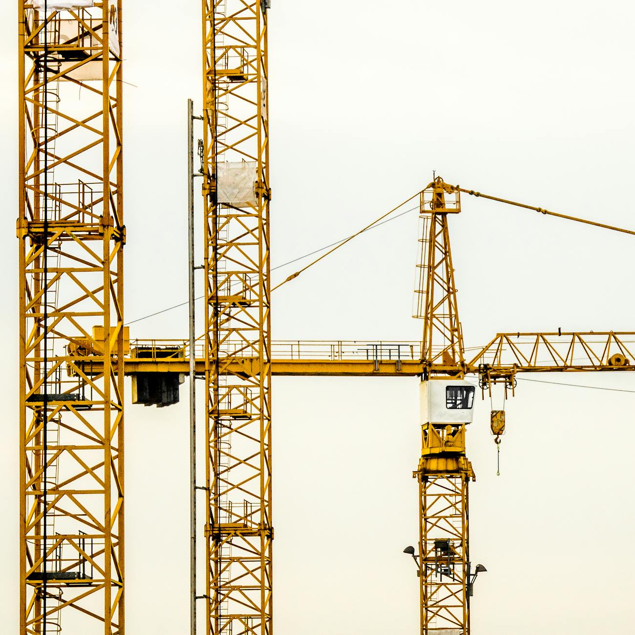 Close-up of yellow construction cranes towering against a pale sky background.